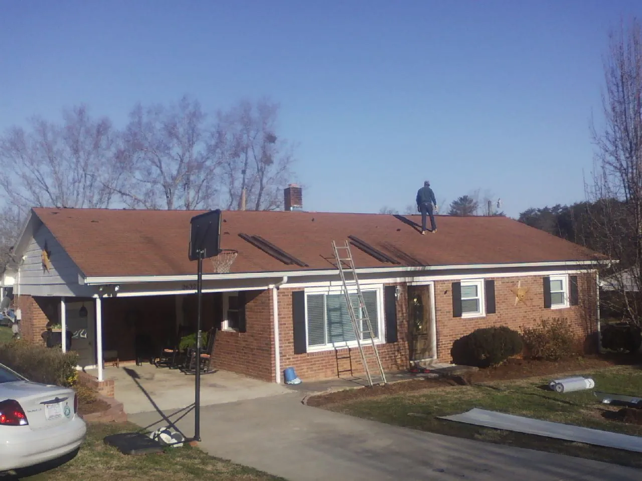 Roofer stripping a shingle roof on a brick ranch before metal panels in Stroudsburg