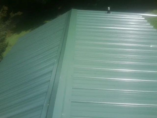 New green metal panels meeting at the ridge of a roof — Flat Roof Repair work by our crew in Stroudsburg