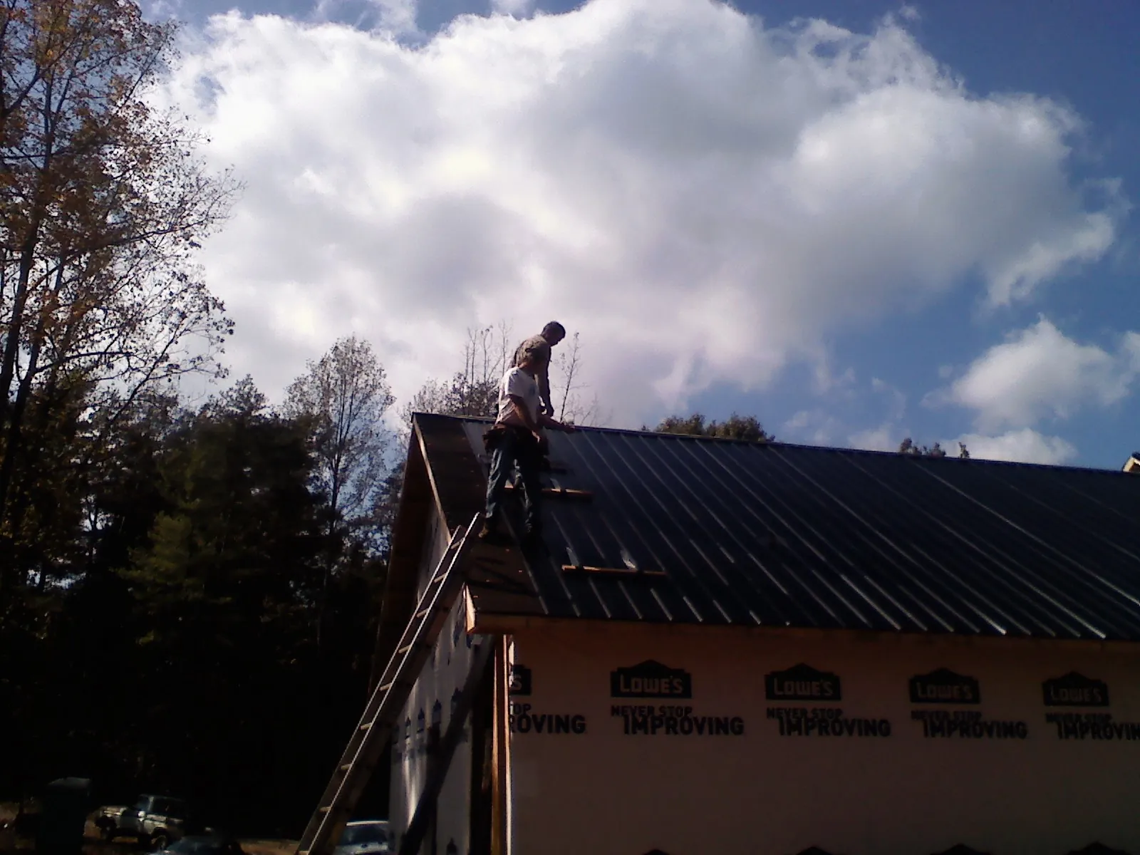 Roofer fastening dark metal panels high against a cloudy sky, from a Roof Inspection job in Stroudsburg