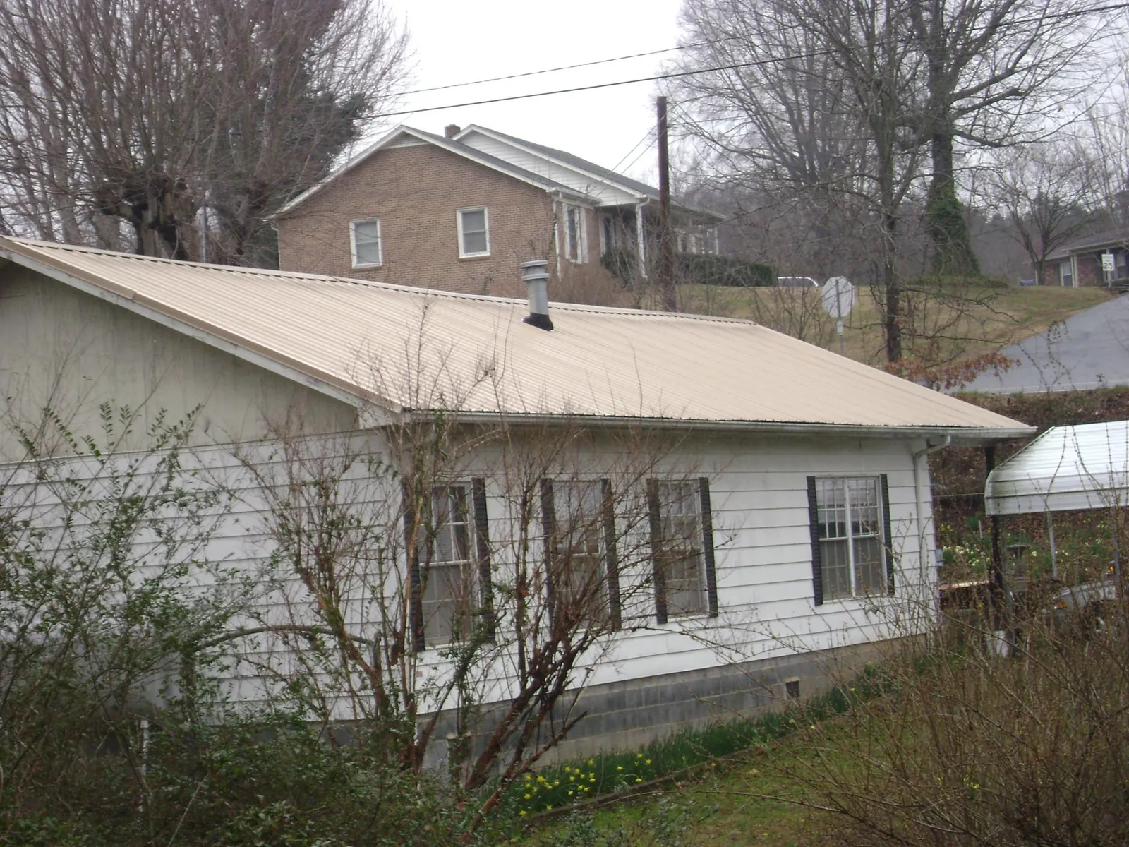 Tan metal roof on a white sided house set into a hillside — Commercial Roofing by Roofing Brothers in Stroudsburg